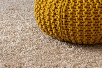 Close-up of plush beige carpet with a yellow knitted pouf — showing the soft texture and comfort that makes carpet the right choice for bedrooms, game rooms, and upstairs spaces